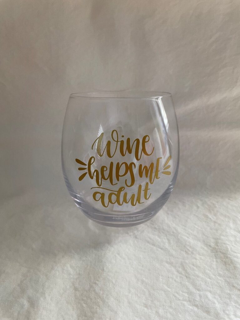 Wine glass with gold lettering and "wine helps me adult" saying