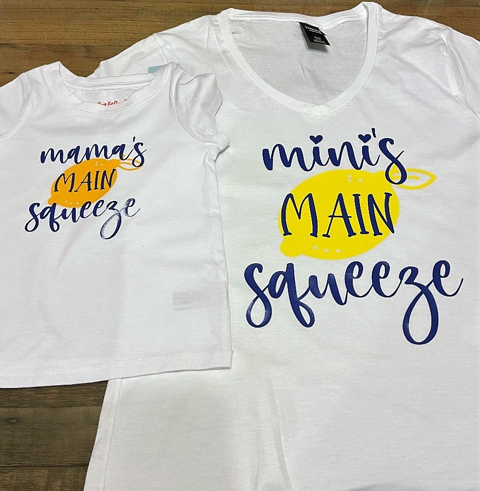 Photo of a toddler sized shirt with the saying "Mama's Main Squeeze" and a lemon overlapping an adult sized shirt with the saying "Mini's Main Squeeze" with a lemon
