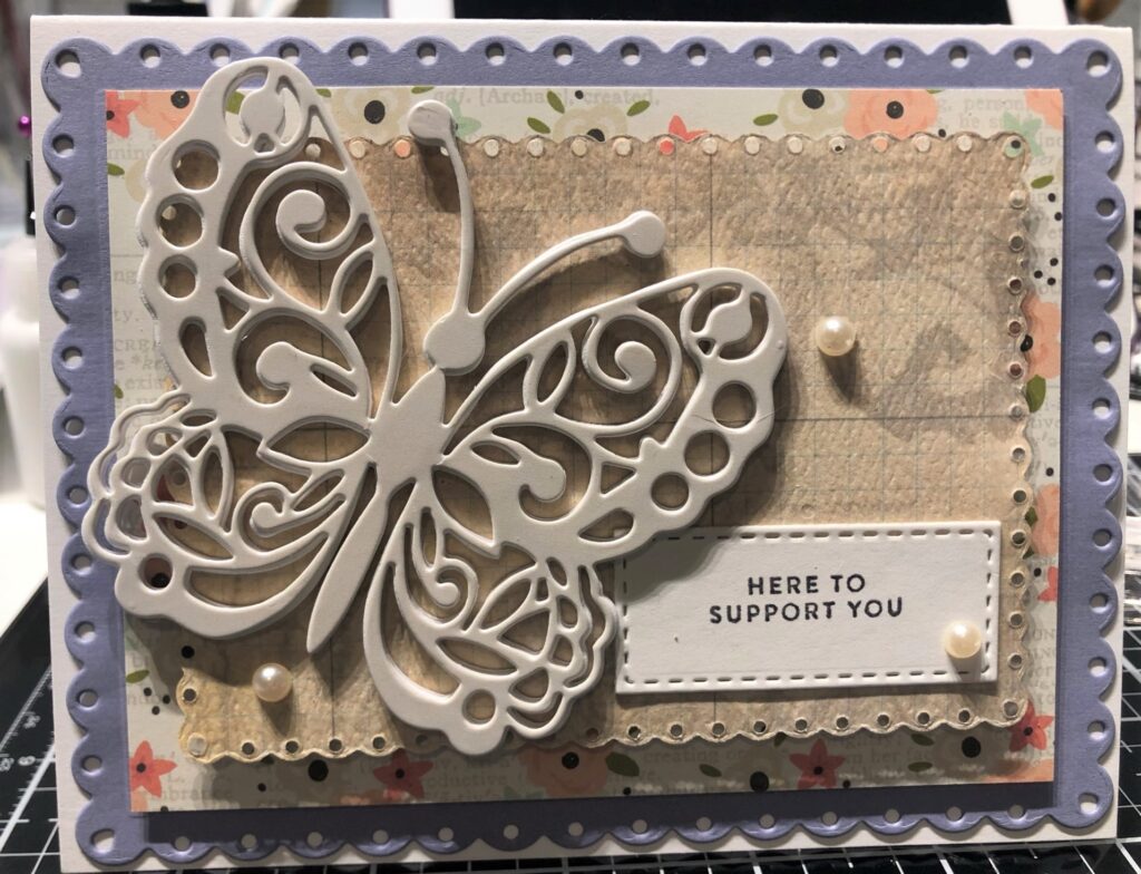 Thinking of you card with a large cream colored butterfly cutout on top of layers of cream, floral, and light purple paper with a small rectangle on lower right that says "here to support you"
