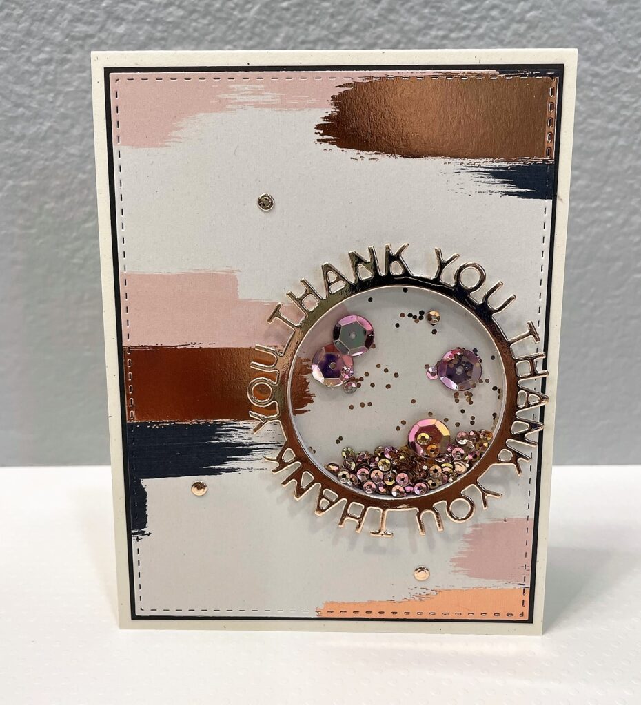 Thank you card with a circle frame repeating thank you thank you thank you around thin circle and shaker with sequins and glitter in the middle on cream paper with paint brush strokes of rose gold, pale pink, and dark gray 
