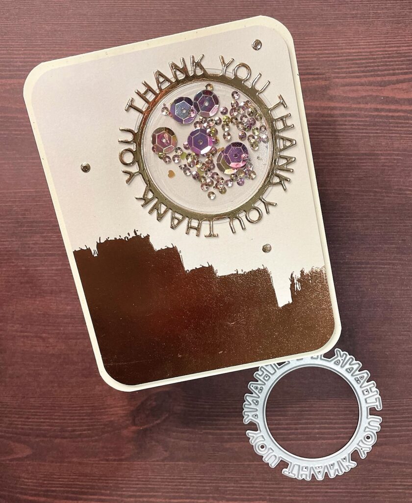 Thank you card with a circle frame repeating thank you thank you thank you around thin circle and shaker with sequins and glitter in the middle on cream paper with rose gold pattern on bottom of paper on top of thank you circle frame die