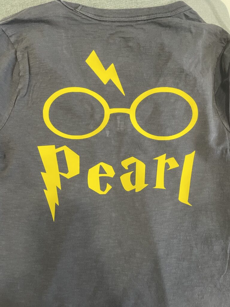 Back of a gray t-shirt with Harry Potter style glasses and Harry Potter lightning bolt scar with the name "Pearl" below them