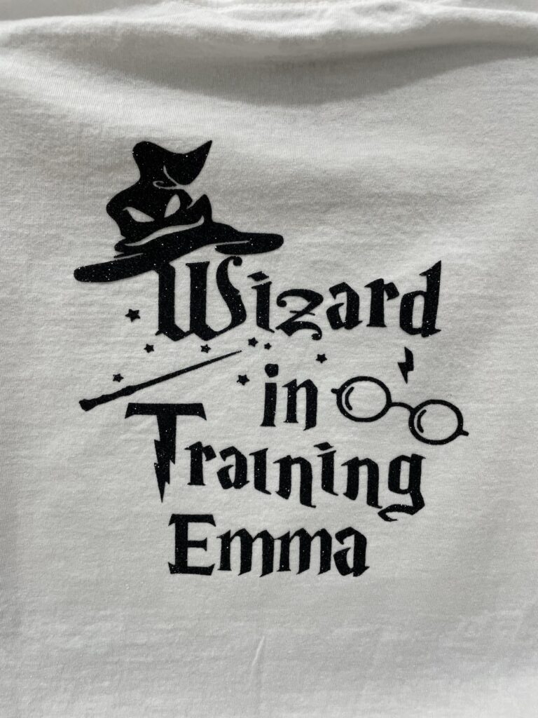 White t-shirt with glitter black design that says Wizard in Training Emma