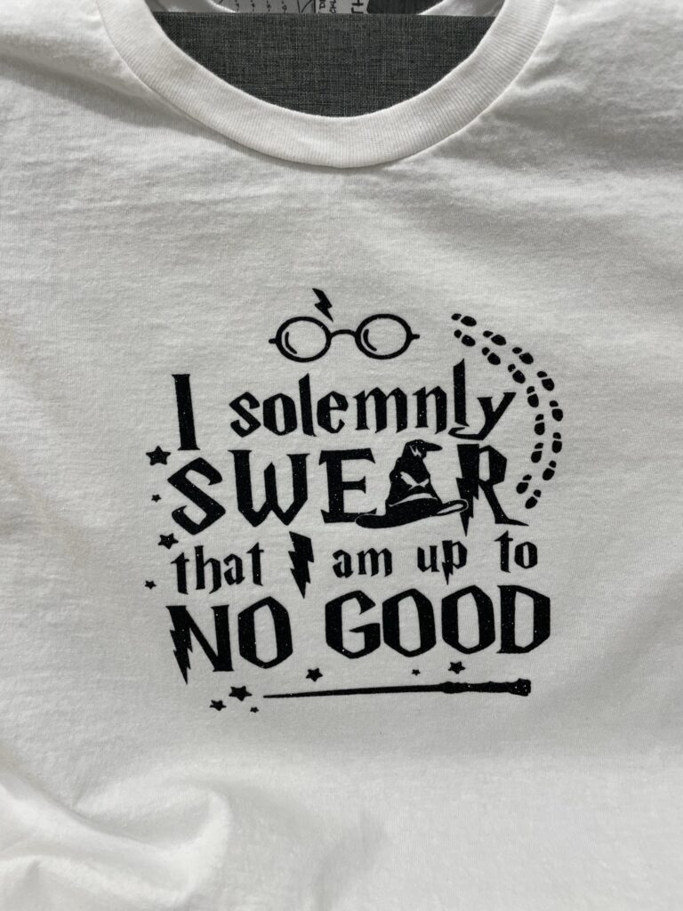 White t-shirt with a sparkly black design that says "I solemnly swear that I am up to no good"