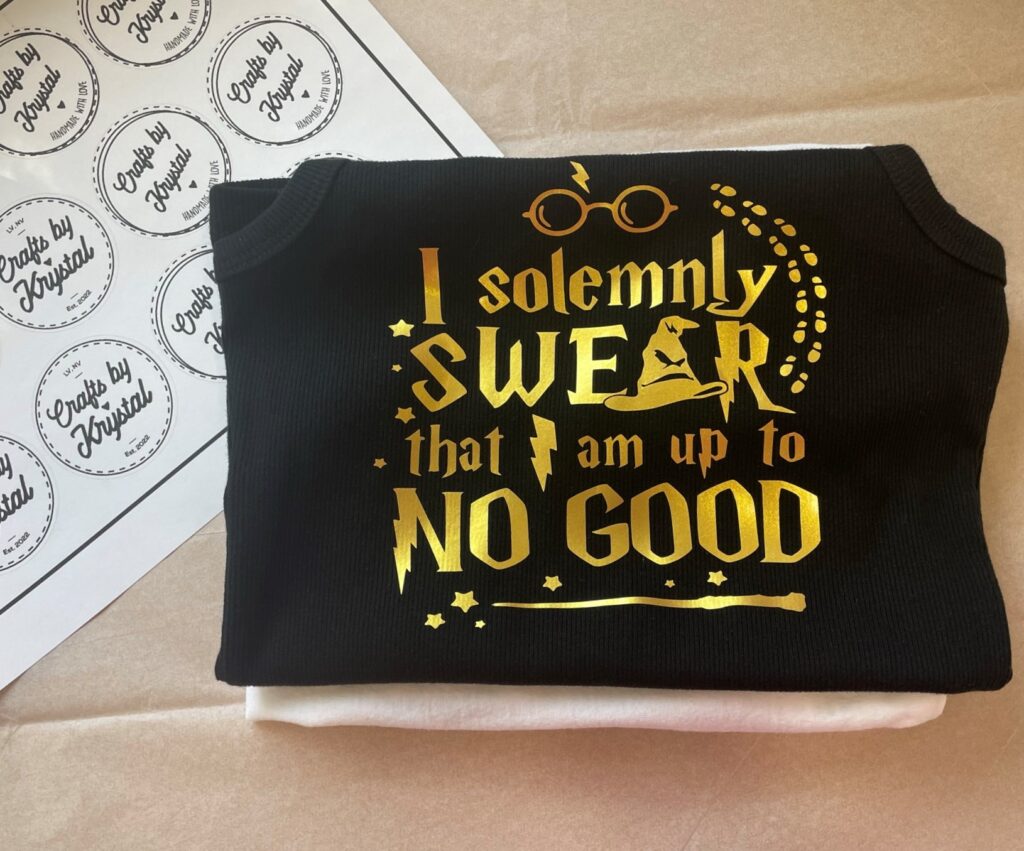 Two folded shirts with black tank top with gold design that says I solemnly swear that I am up to no good and white and black stickers on the left hand side that say Crafts by Krystal