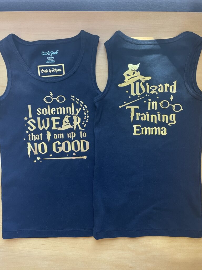 Picture of two black tank tops with gold designs that say "I solemnly swear that I am up to no good" on the front and "wizard in training Emma" on the back